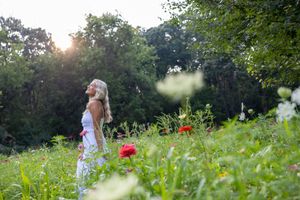 A white sundress flows in a summer meadow filled with wildflowers and poppies as sunlight filters through trees.