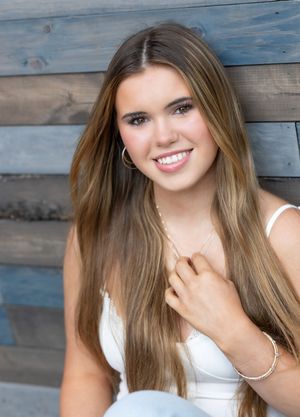 Portrait photo against rustic blue wood paneled wall wearing a white sleeveless top.