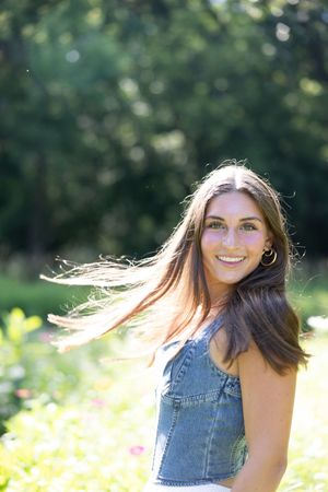 A person in a denim top poses outdoors in a sunny field with flowing hair and natural lighting.