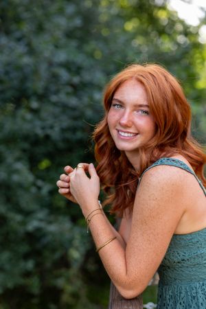 A woman with red hair in a green dress laughs joyfully while posing outdoors against a blurred natural background.