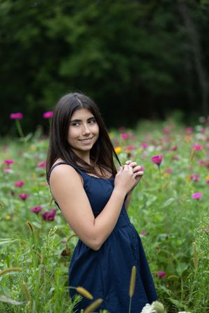 A person in a navy blue dress poses among vibrant pink wildflowers in a lush garden setting.