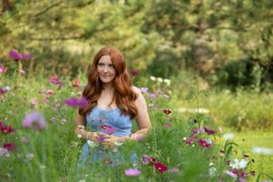 A person in a blue dress stands among blooming pink cosmos flowers in a summer garden.