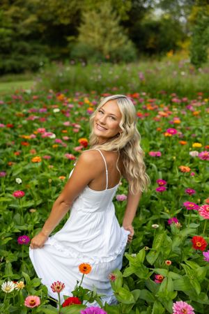 Woman in white sundress sitting gracefully among vibrant zinnias and wildflowers in a summer garden.