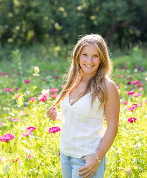 Woman in white dress smiling in a vibrant flower field with pink and yellow blooms during golden hour.