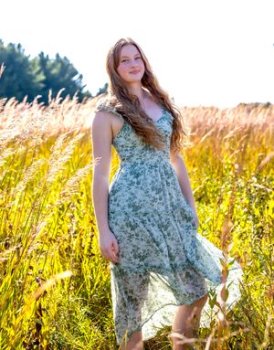 A figure in a floral dress poses gracefully in a sunlit field of tall golden grass during golden hour.