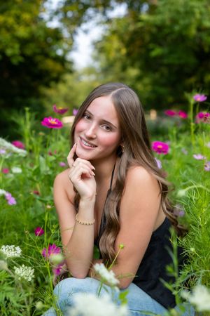 A person sits in a garden surrounded by vibrant pink cosmos flowers on a sunny summer day.