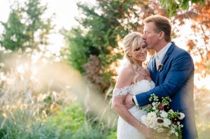 A couple shares a romantic moment in golden sunlight outdoors with white floral bouquet and navy blue suit.