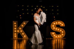 A romantic couple dances in front of illuminated marquee letters K and S at their wedding reception.