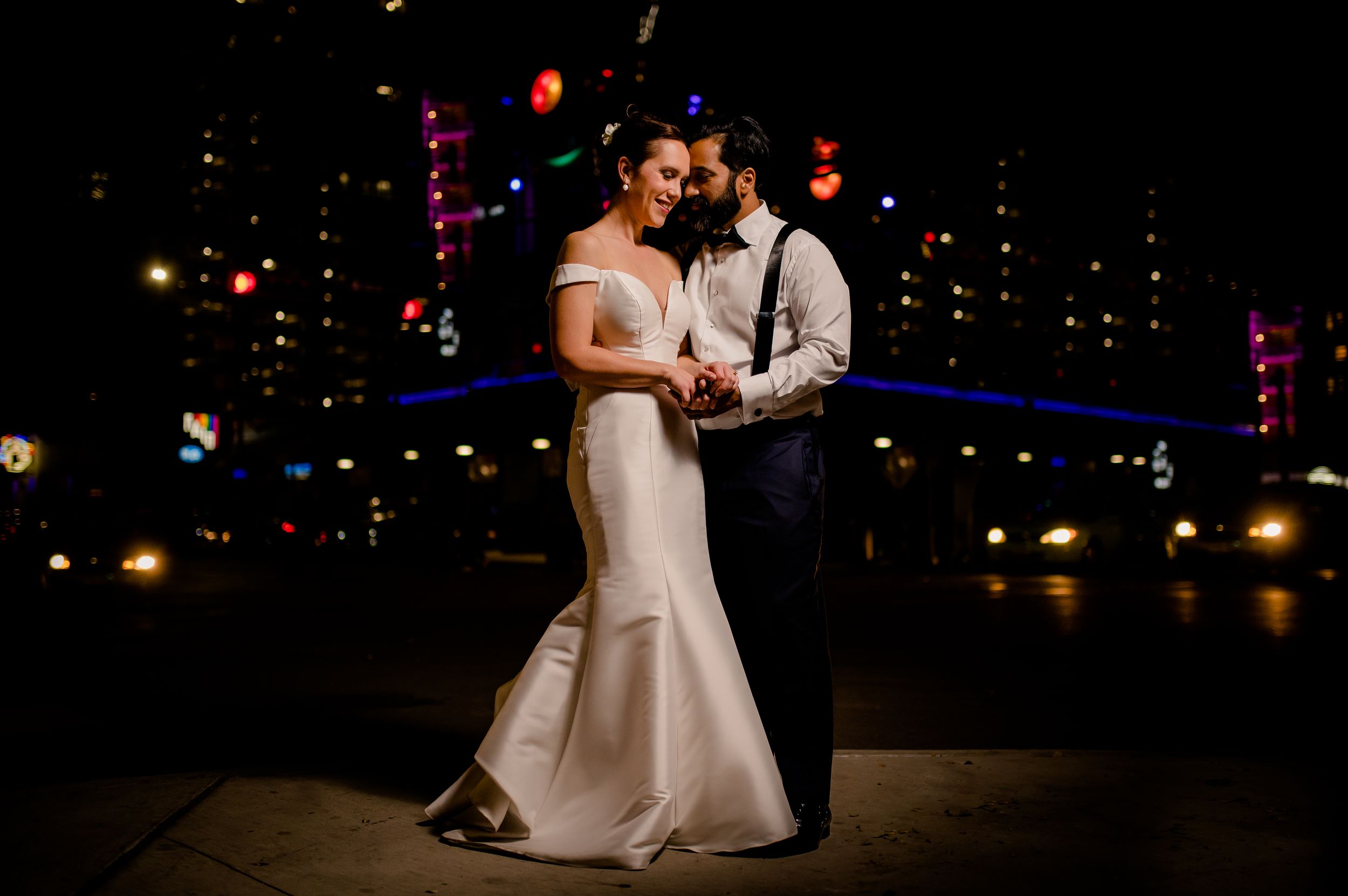Dancing couple in formal attire share an intimate moment under twinkling lights at night.
