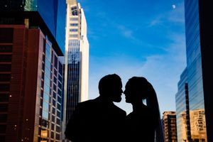Silhouette of two romantic figures sharing an intimate moment against a backdrop of urban skyscrapers and blue sky.