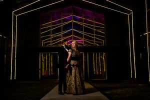 A couple in formal attire embraces under illuminated geometric arches at a nighttime wedding venue.