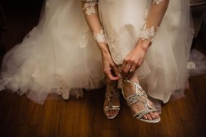 A bride in a tulle wedding dress adjusts her silver strappy sandals while preparing for her special day.