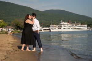 Two people embracing on a beach shore with a riverboat cruise ship visible in the background.
