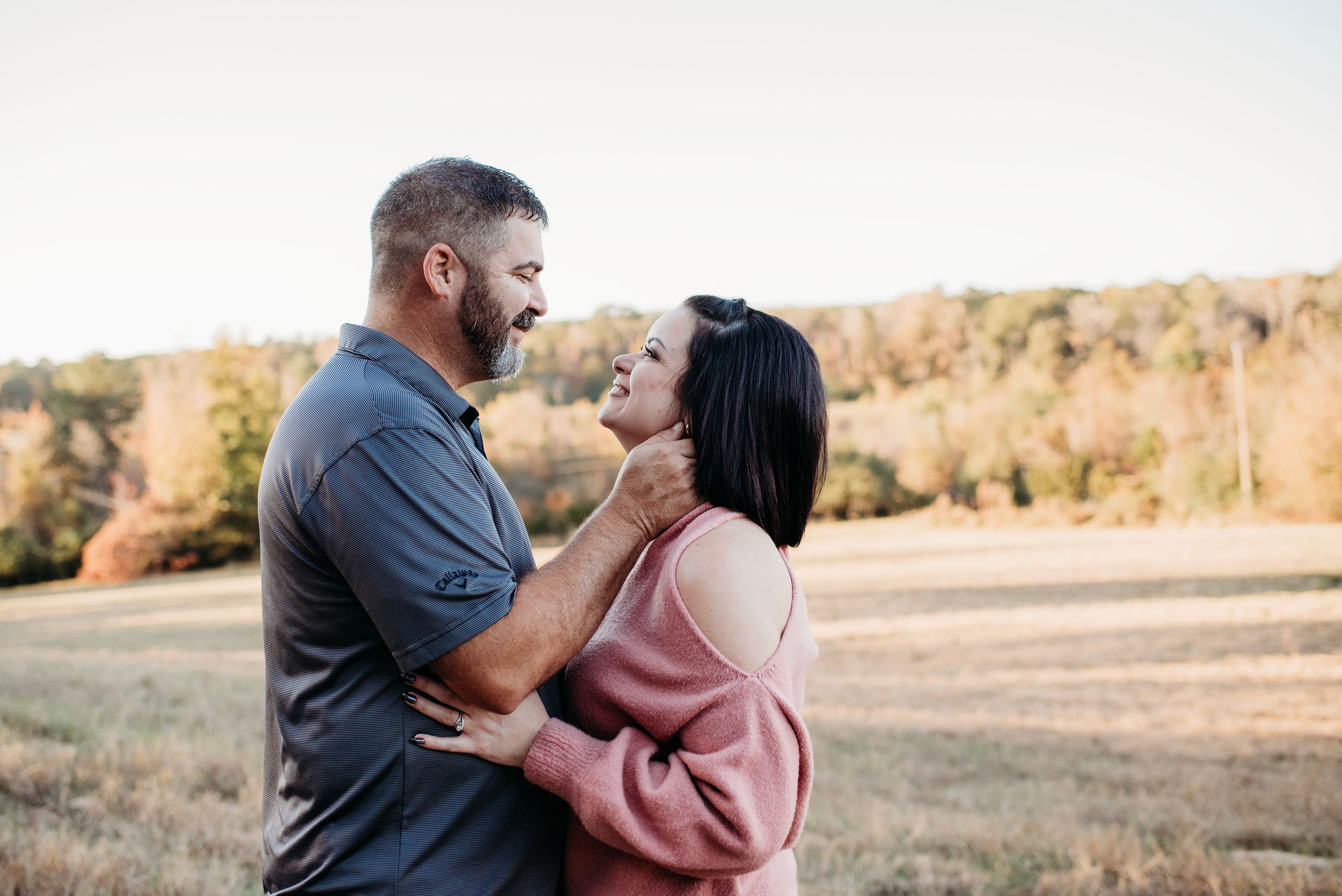 Couple embraces and laughs together in a golden autumn field during sunset.