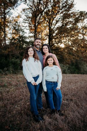 A family poses together in a golden field at sunset wearing coordinated blue jeans and light colored tops.