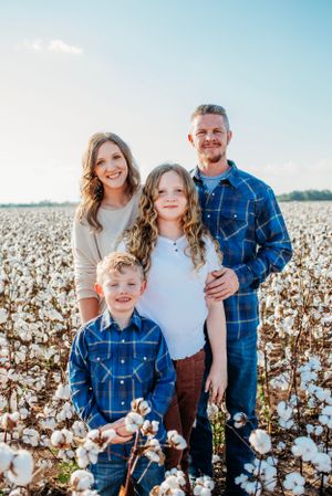 Family wearing coordinated blue and white outfits poses together in a cotton field.