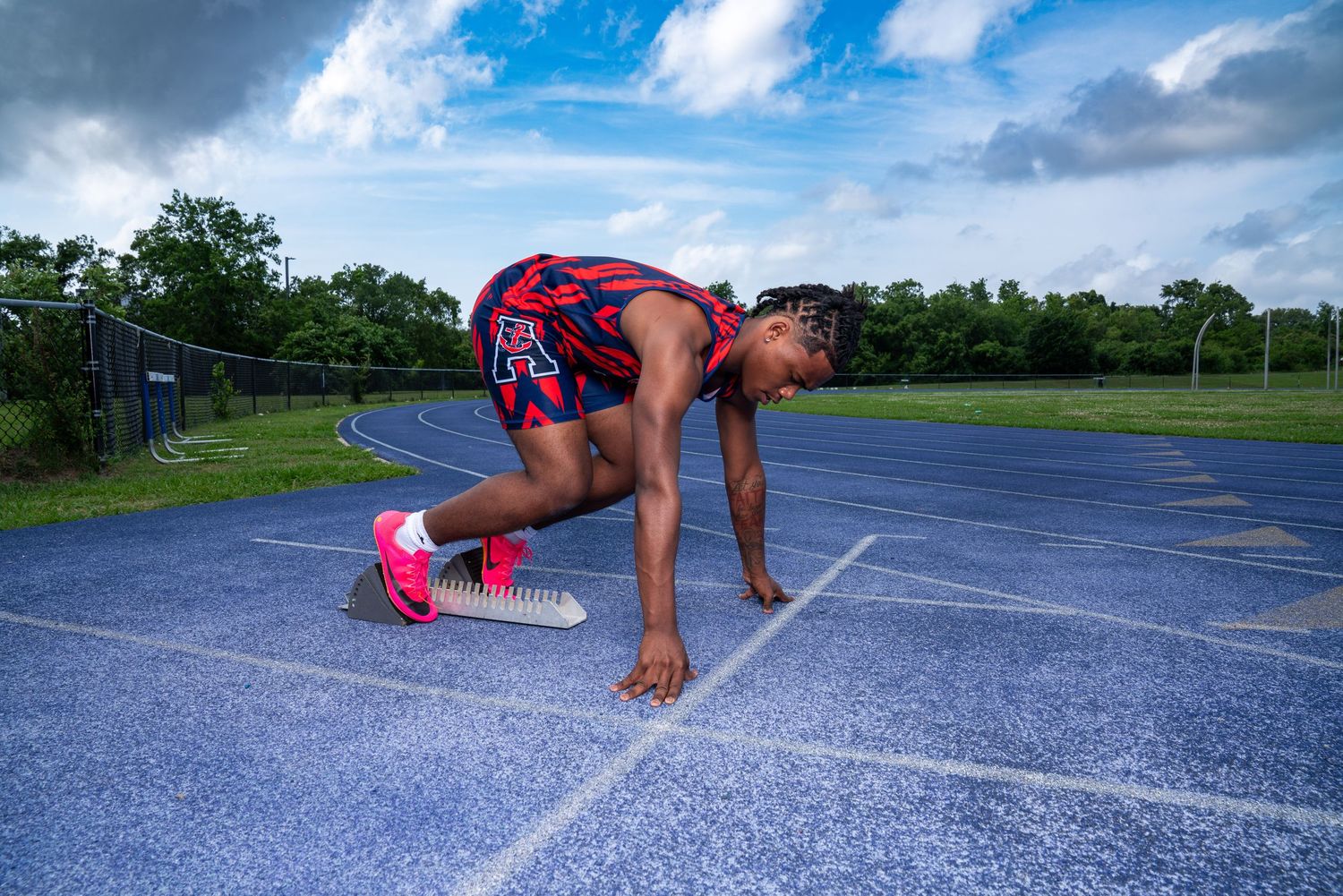 Athletic person performing a burpee exercise sequence on an outdoor track with cloudy sky overhead.