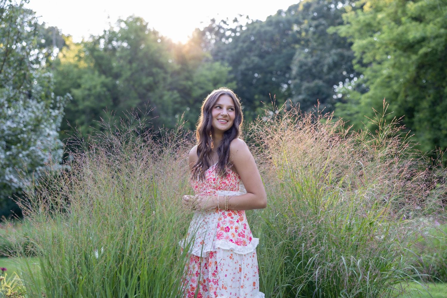 Woman in orange dress poses by white fence with natural background.