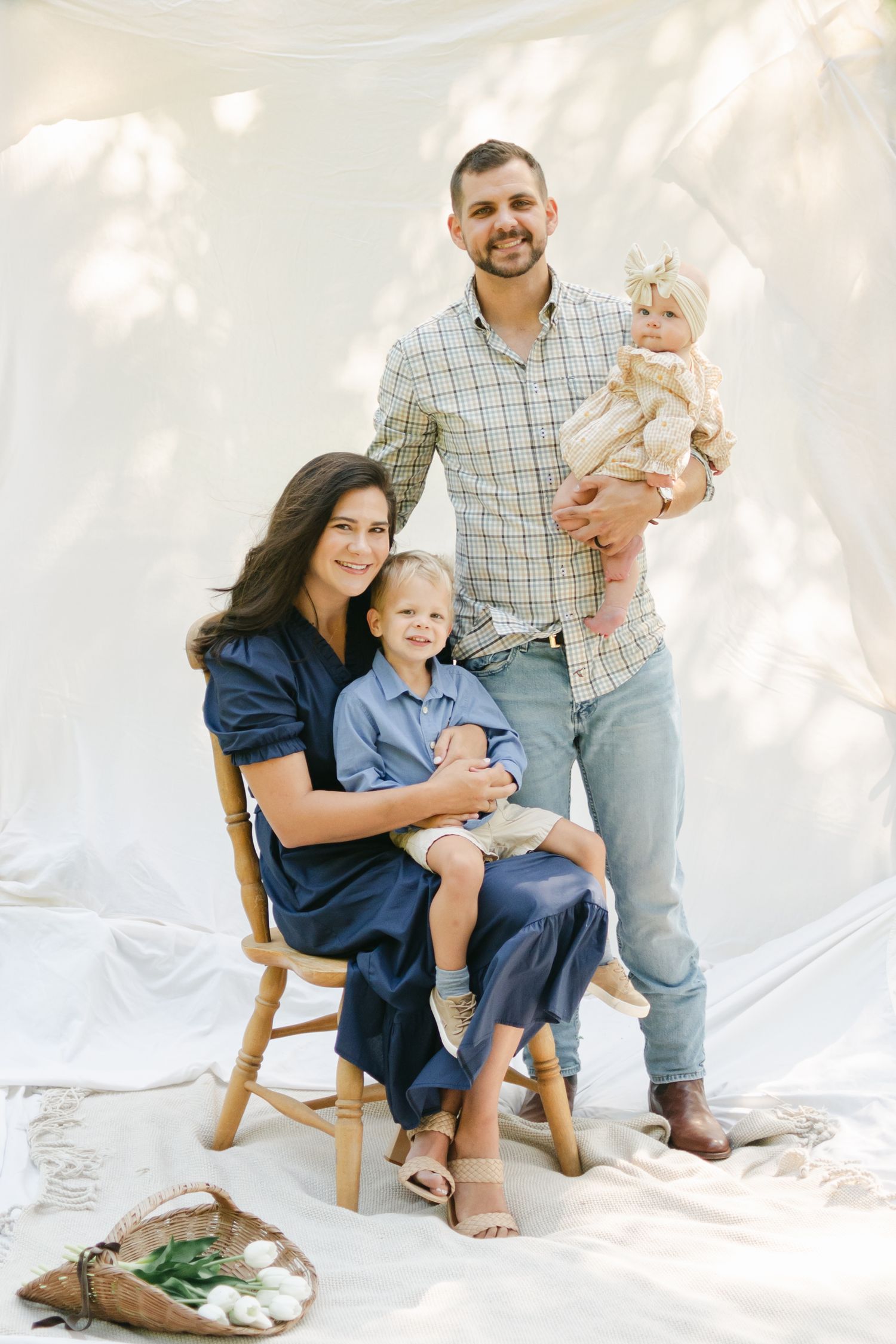 A smiling family of four poses together in a bright studio with white draping.