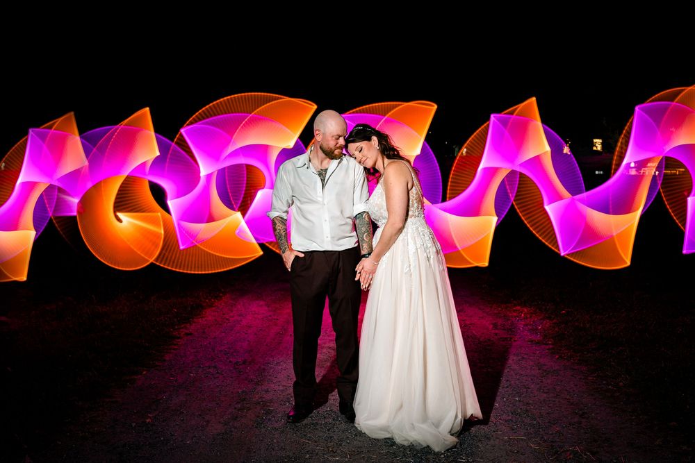 Wedding couple dances on dark floor surrounded by glowing pink and orange balloon light installations.