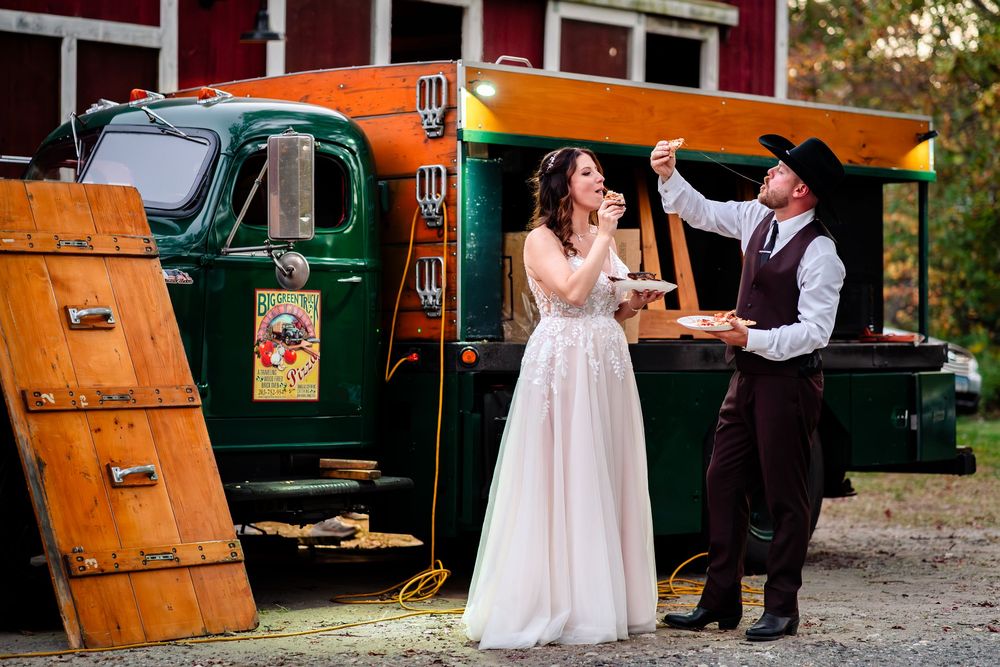 A couple shares a moment beside a vintage green and orange food truck at an outdoor venue.
