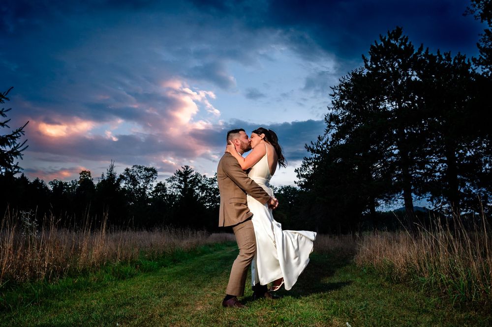 Silhouetted couple dancing in a field against a dramatic sunset sky with wispy pink clouds.