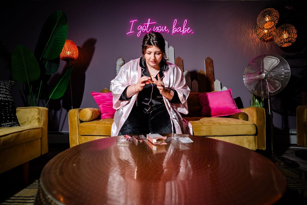 A person sits on a couch under pink neon lighting with a round wooden table in the foreground.