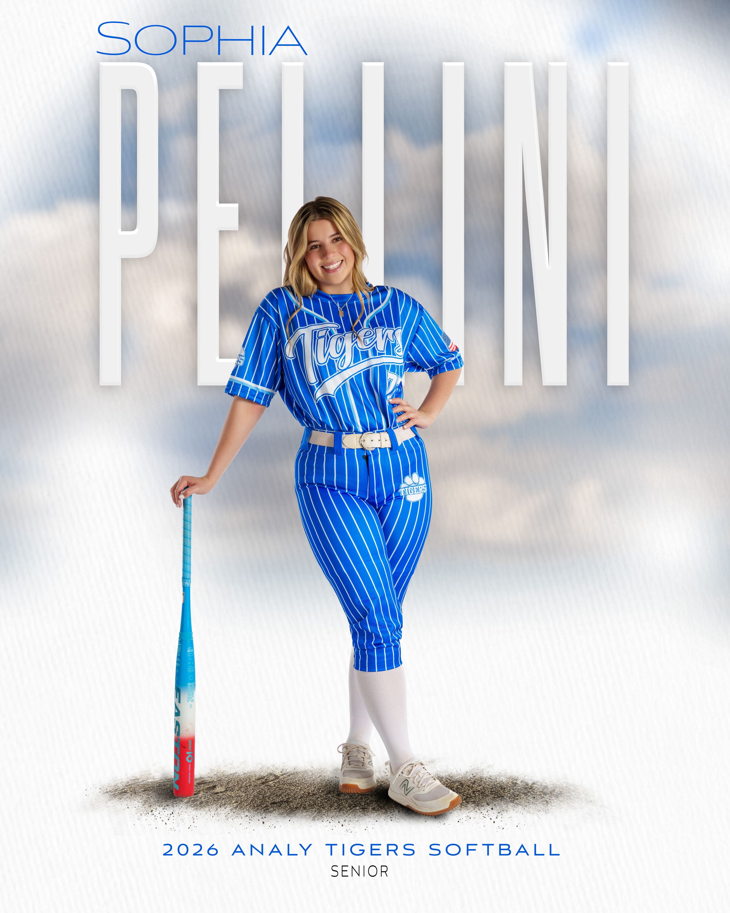 A softball player poses in a blue pinstriped uniform with a bat against a cloudy background for a sports portrait.