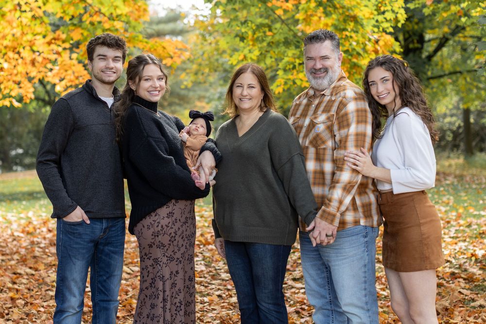 Family of six posing outdoors among vibrant autumn foliage, smiling together in a warm fall setting.