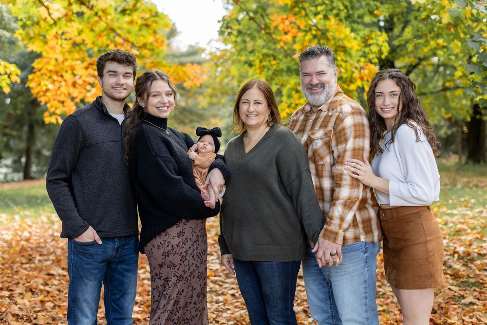 Family of six posing together in autumn park with colorful fall foliage backdrop.