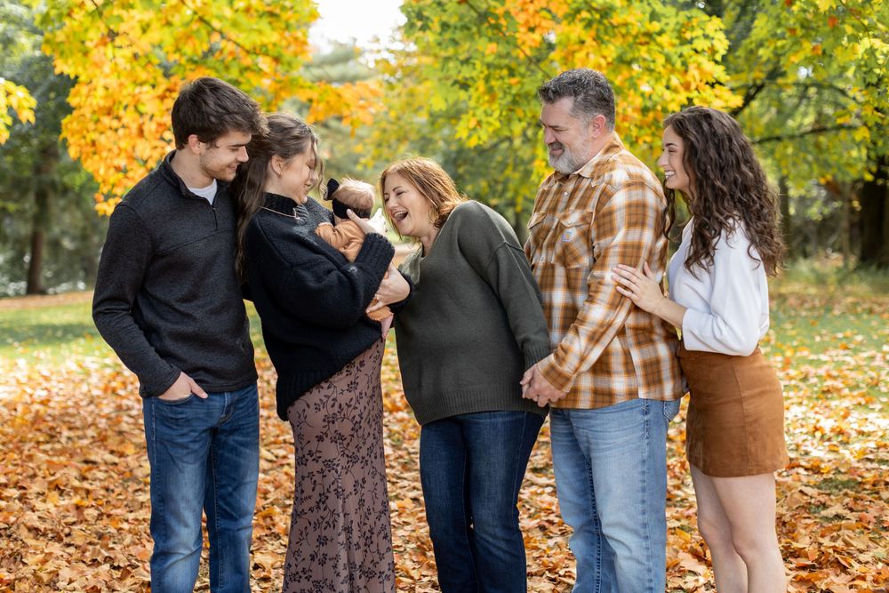 Joyful family of six laughing together among golden fall leaves in a park.