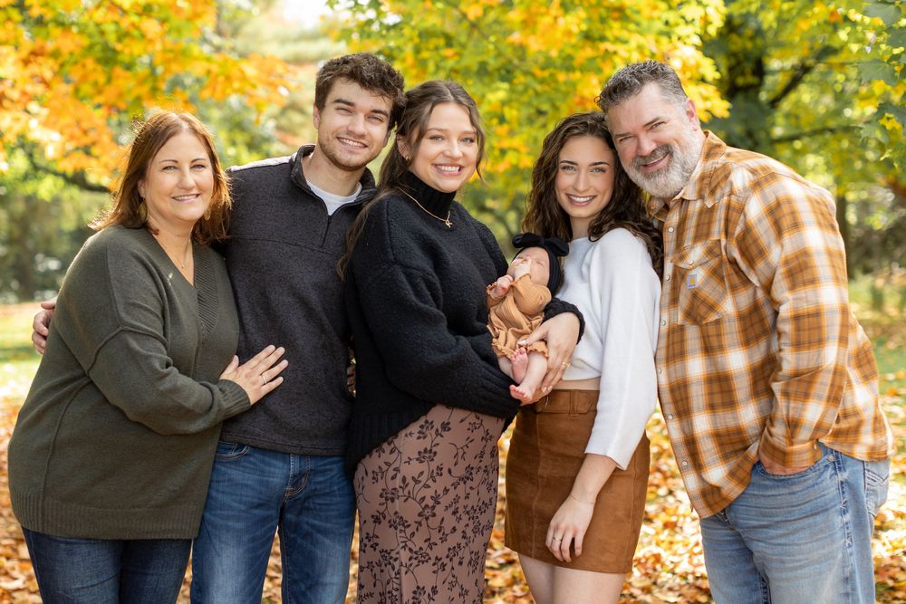 Family of five smiling together outdoors among vibrant autumn foliage in a warm fall photo session.