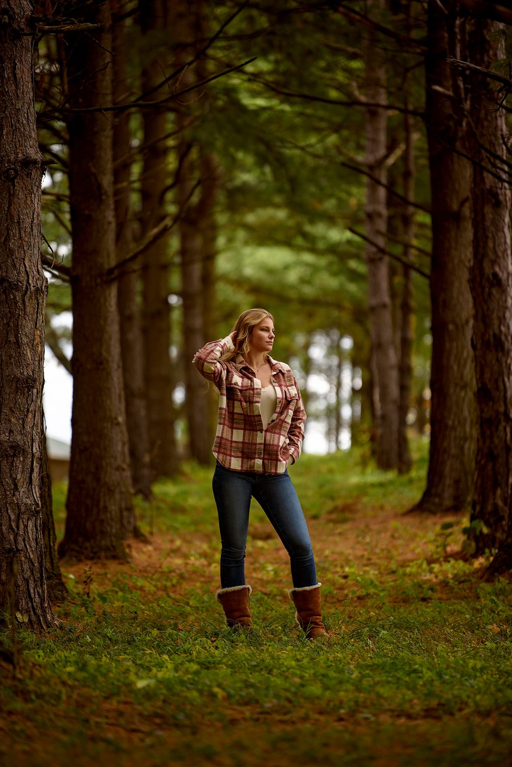 Person in plaid shirt and jeans walking through pine forest in autumn.