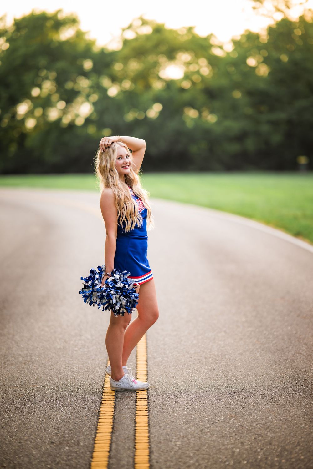 Cheerleader in blue uniform poses on yellow road lines during golden hour photoshoot.
