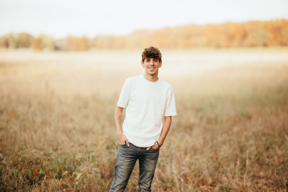 A person in a white t-shirt and jeans stands in a golden wheat field during sunset.
