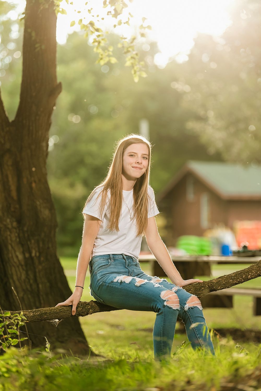 Golden hour portrait session on a mossy tree branch in ripped jeans and casual white top.