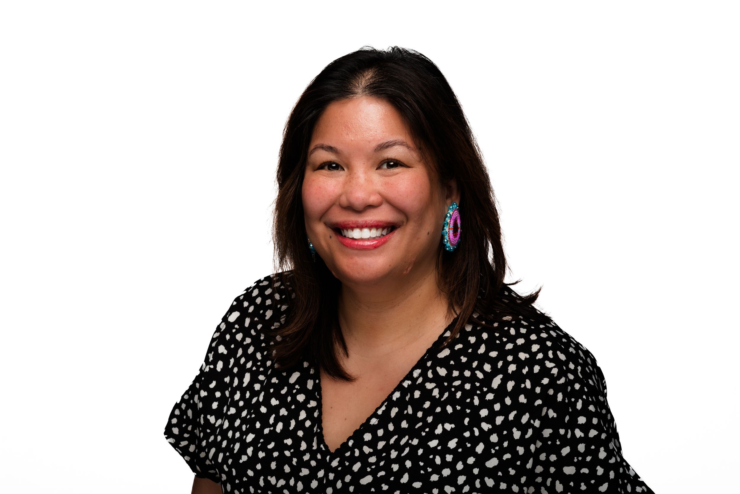 Professional portrait of someone wearing a black and white polka dot top with turquoise earrings against a white backdrop.
