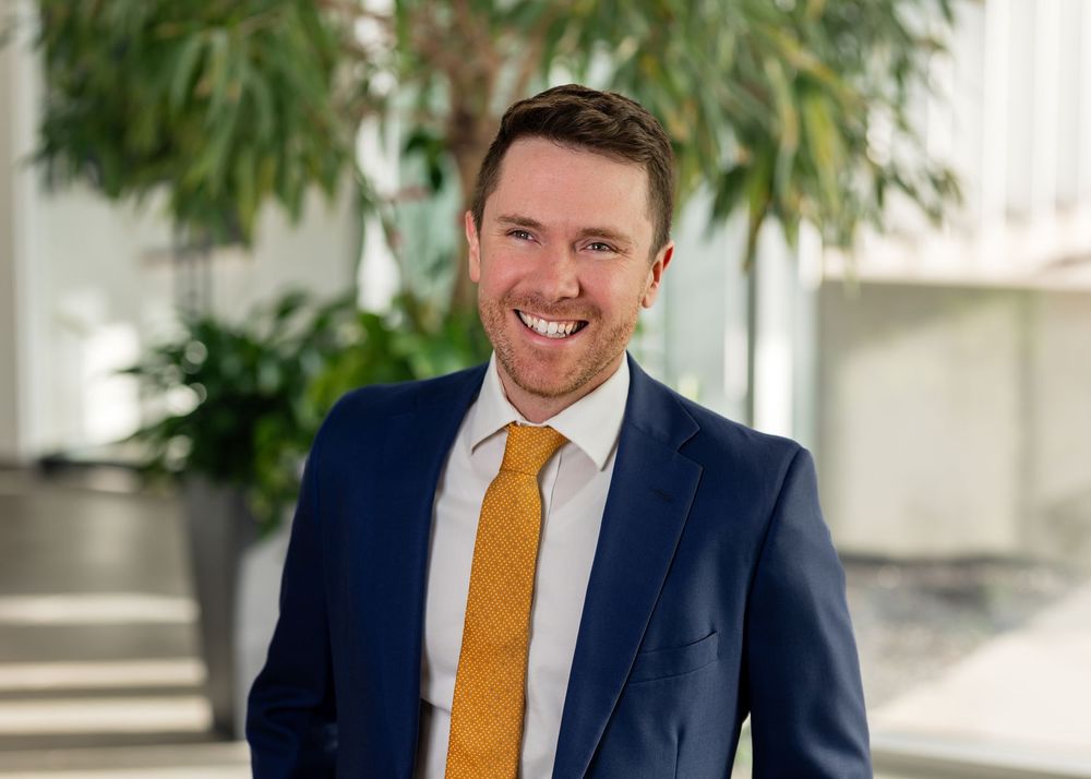 Professional headshots of a person in a navy suit with yellow tie against a bright background.