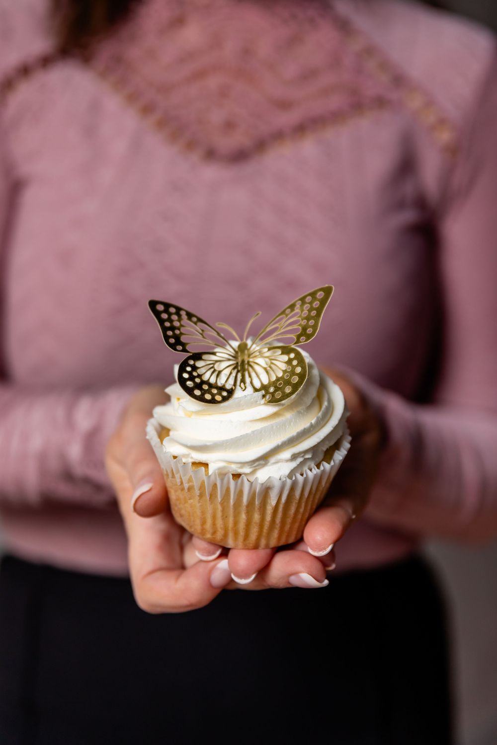 Cupcake with butterfly decoration and white frosting held against pink sweater.