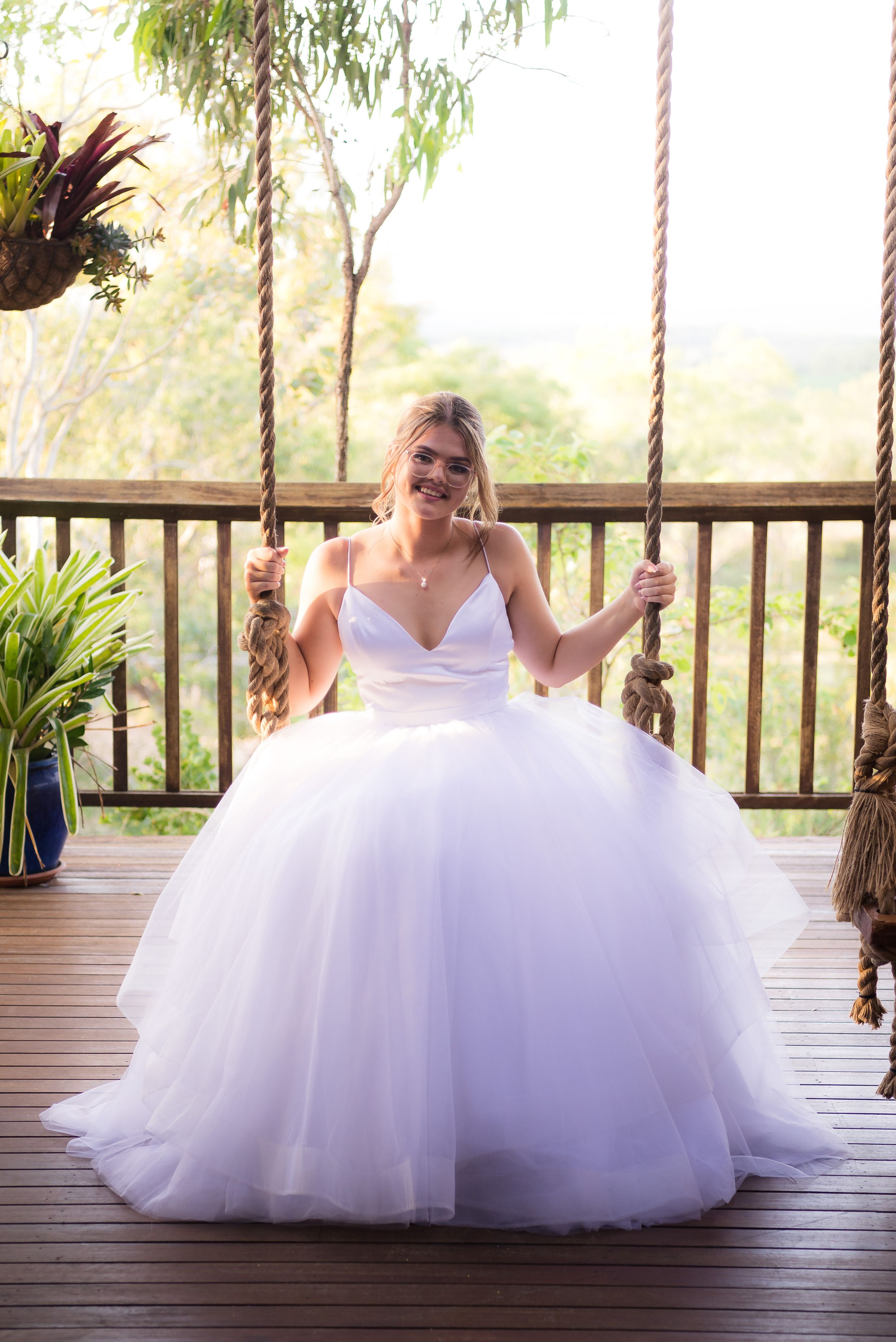 A bride in a voluminous white tulle wedding gown sits on a deck swing in five different poses.