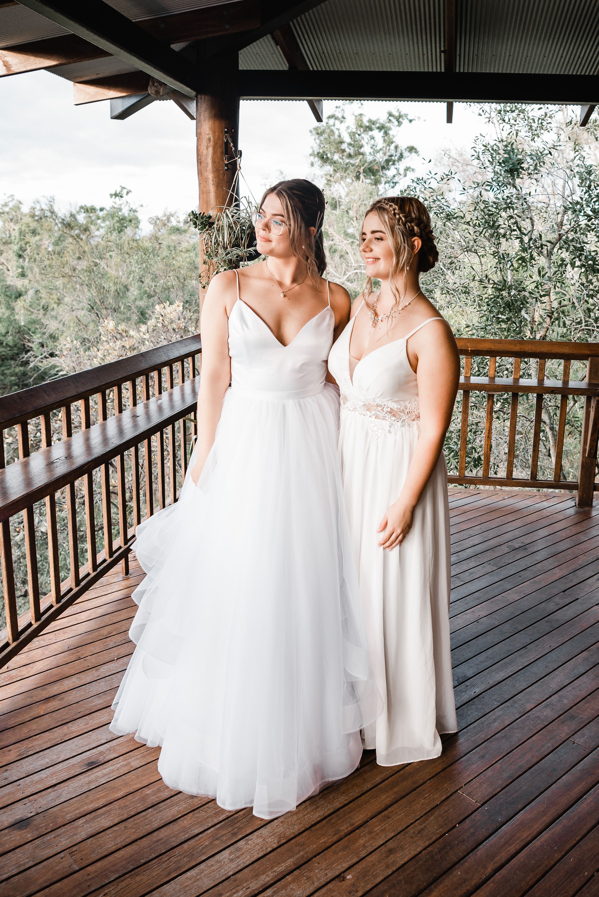 A bride and bridesmaid share a joyful moment together on a rustic wooden deck during a wedding celebration.
