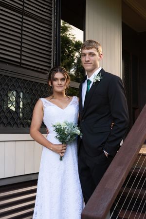 A formal couple poses on wooden steps, with the bride in white lace and groom in black suit.
