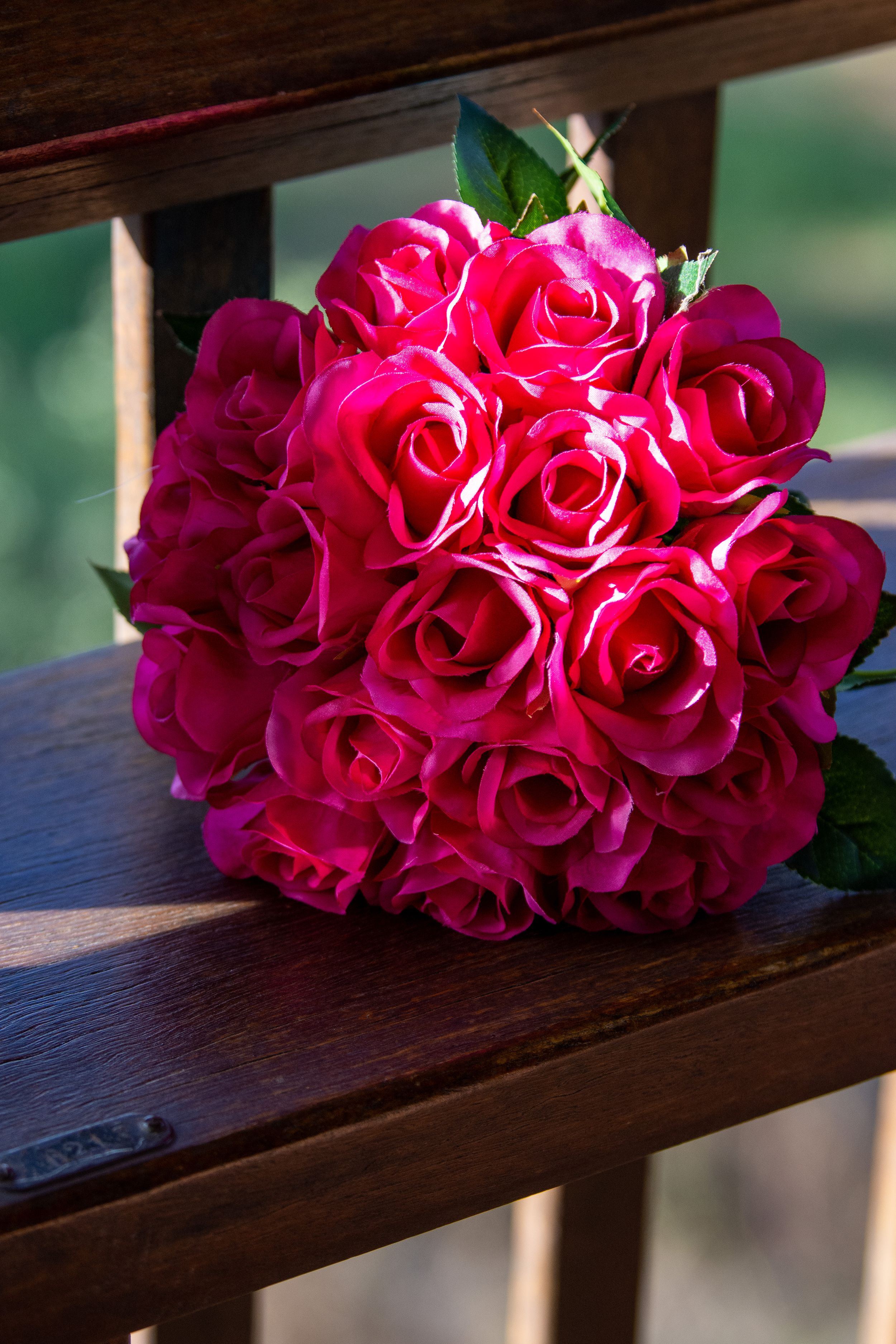 A cluster of vibrant hot pink roses resting on a rustic wooden railing in natural lighting.