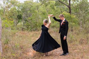 Two people in formal attire sharing a playful moment outdoors.