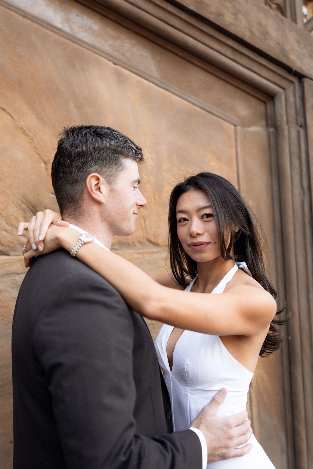 A romantic couple shares an intimate moment against a stone wall background.