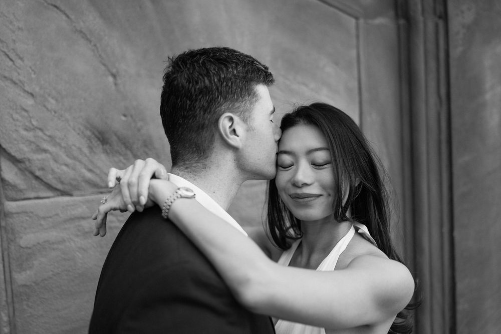 A couple embraces tenderly in front of a textured stone wall.