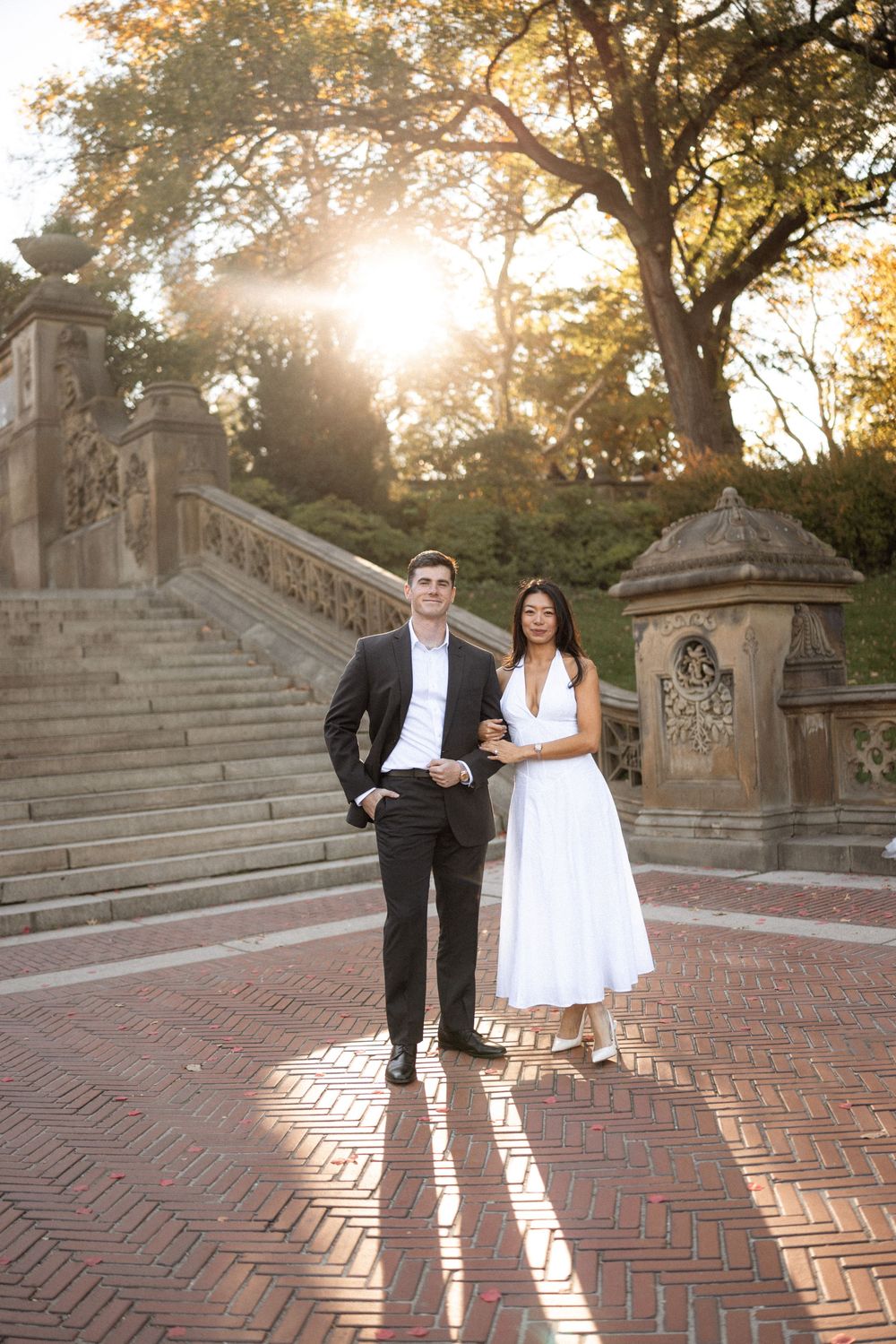 A couple poses playfully on brick steps during golden hour sunset.