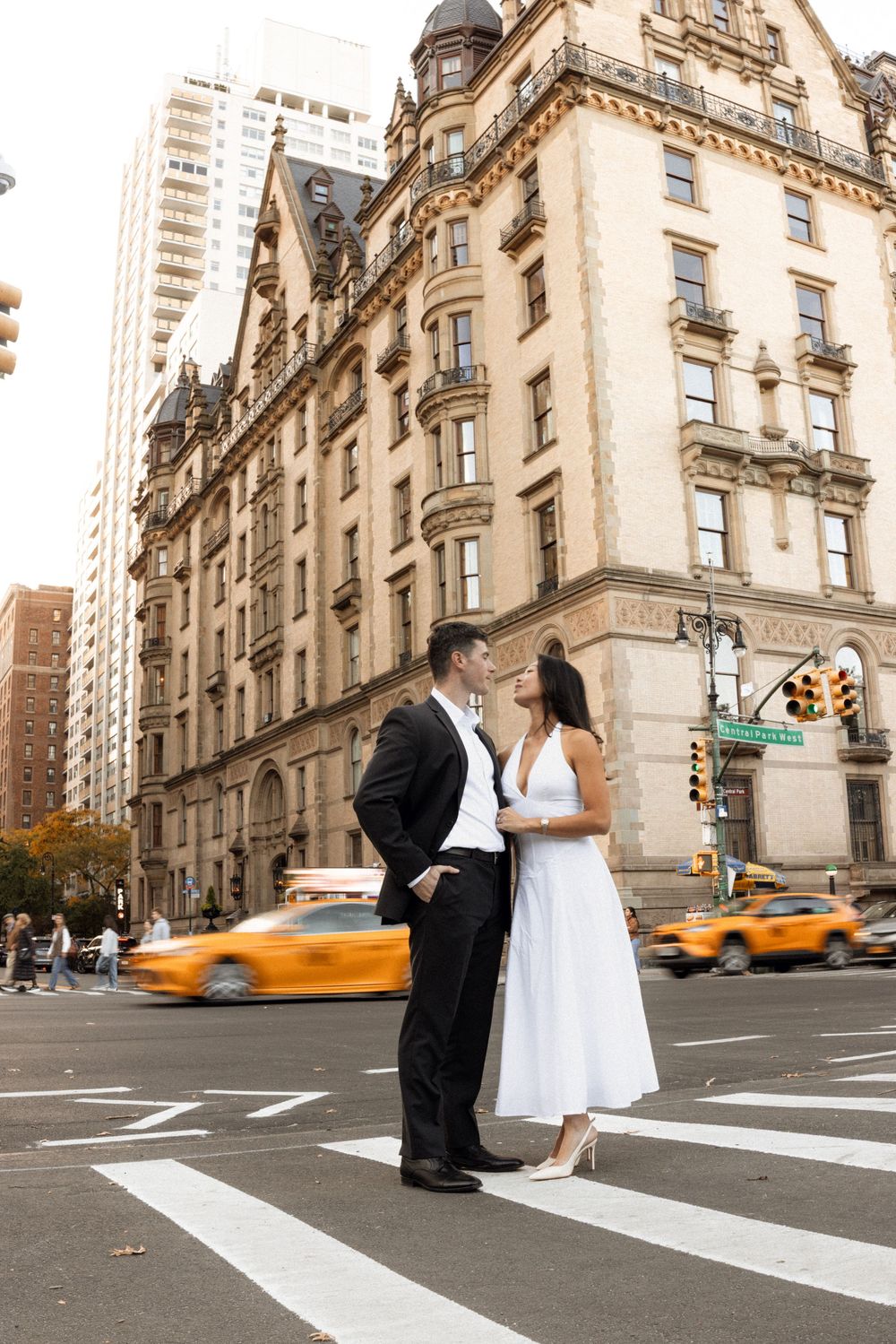 A couple stands together on a city crosswalk with yellow taxis in the background.