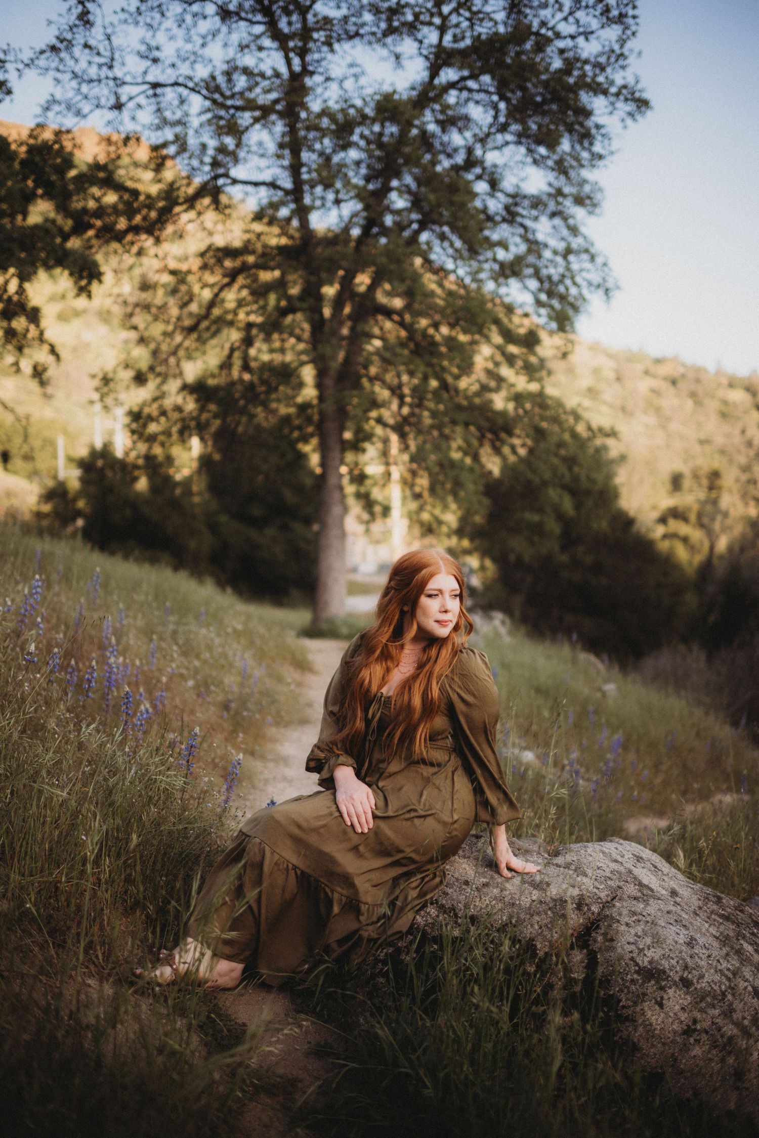 Portrait of someone in a brown dress sitting on a rock during golden hour.