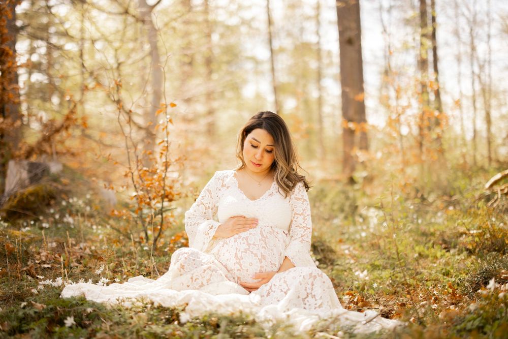 Glowing autumn scene in a forest with someone wearing a flowy white lace dress sitting among fallen leaves.